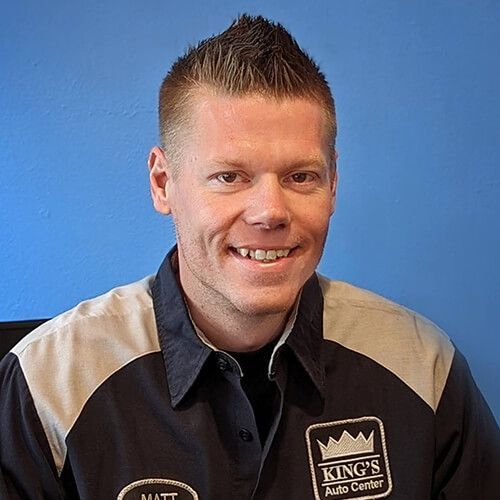 Man with a spiked haircut smiles in an auto shop uniform. The shop is King's Auto Center.
