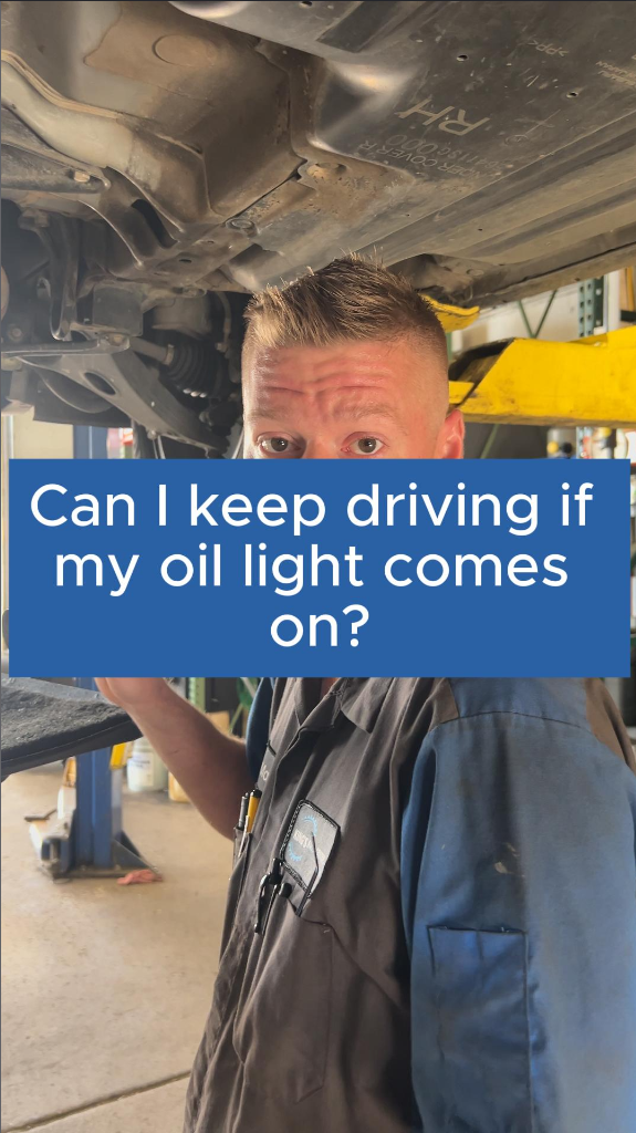 Mechanic under car, asking if driving with oil light on is safe. Auto shop setting.