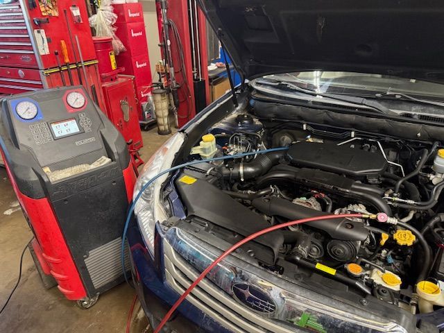 Car engine being serviced with an air conditioning machine in a garage. Blue and red hoses connect to the vehicle. | King's Auto Center