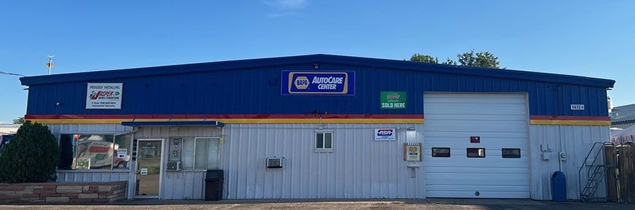 A blue auto repair shop with white metal siding and a large garage door, featuring a phone number and shop name on the exterior. | King's Auto Center