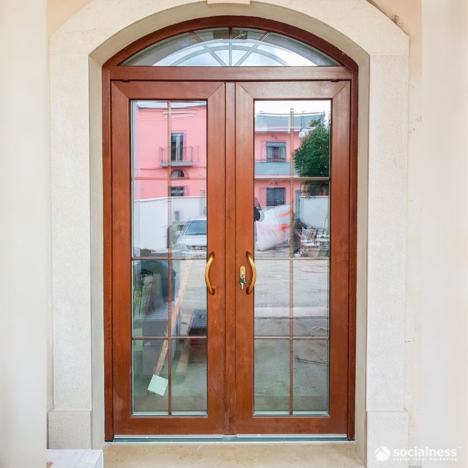 Doppie porte marroni con pannelli in vetro e una finestra semicircolare nella parte superiore, che riproduce una scena di strada.