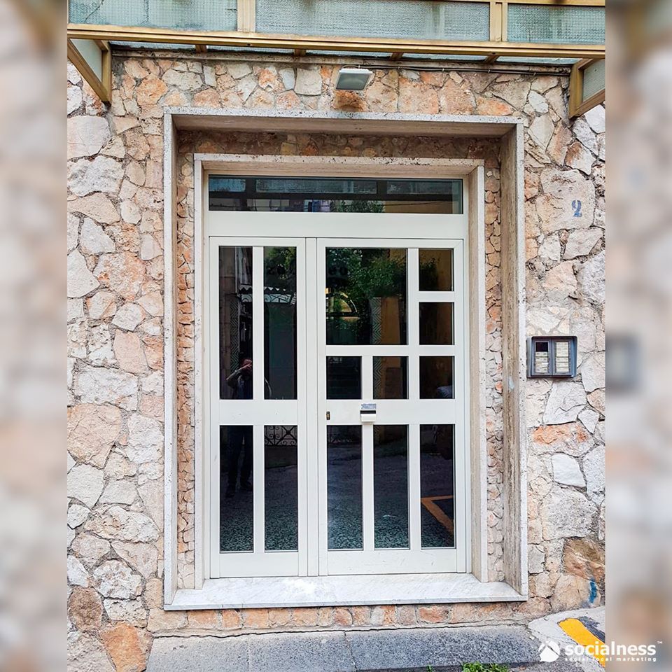 Doppie porte bianche con vetri incastonati in una facciata in pietra.