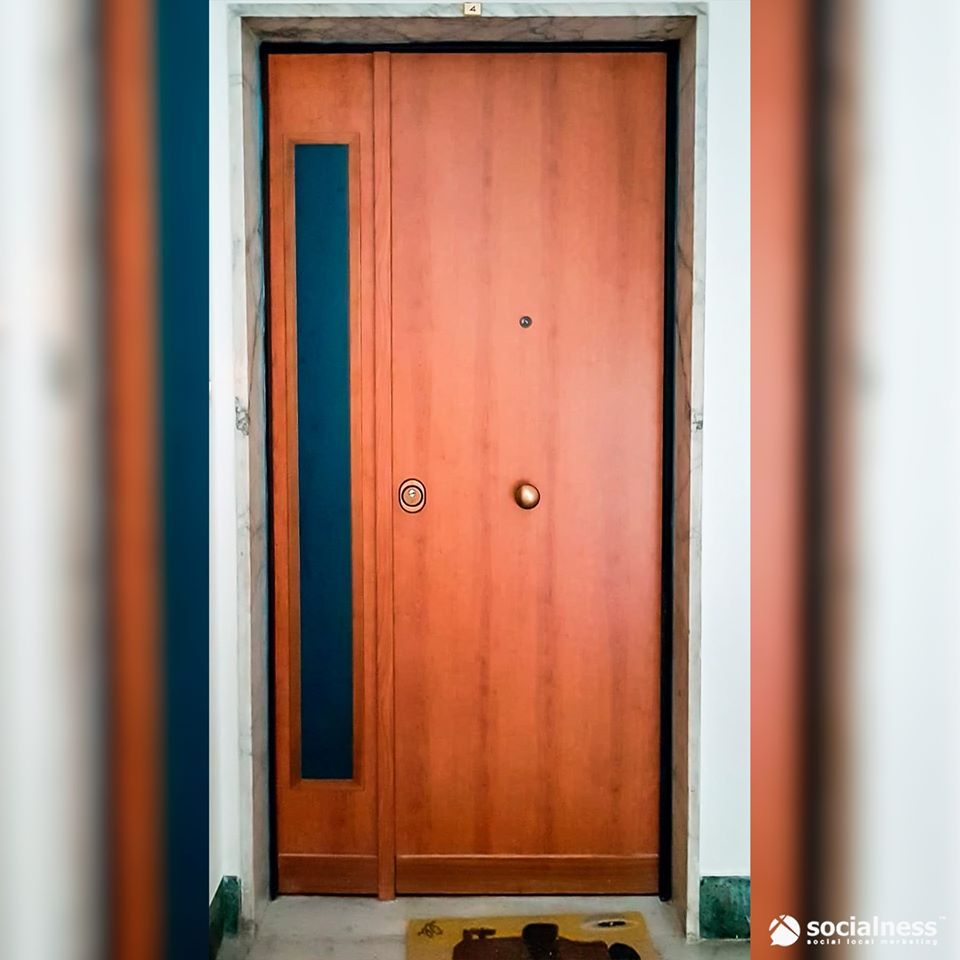 Porta d'ingresso in legno con finestra laterale. Telaio scuro, ferramenta in ottone e zerbino.