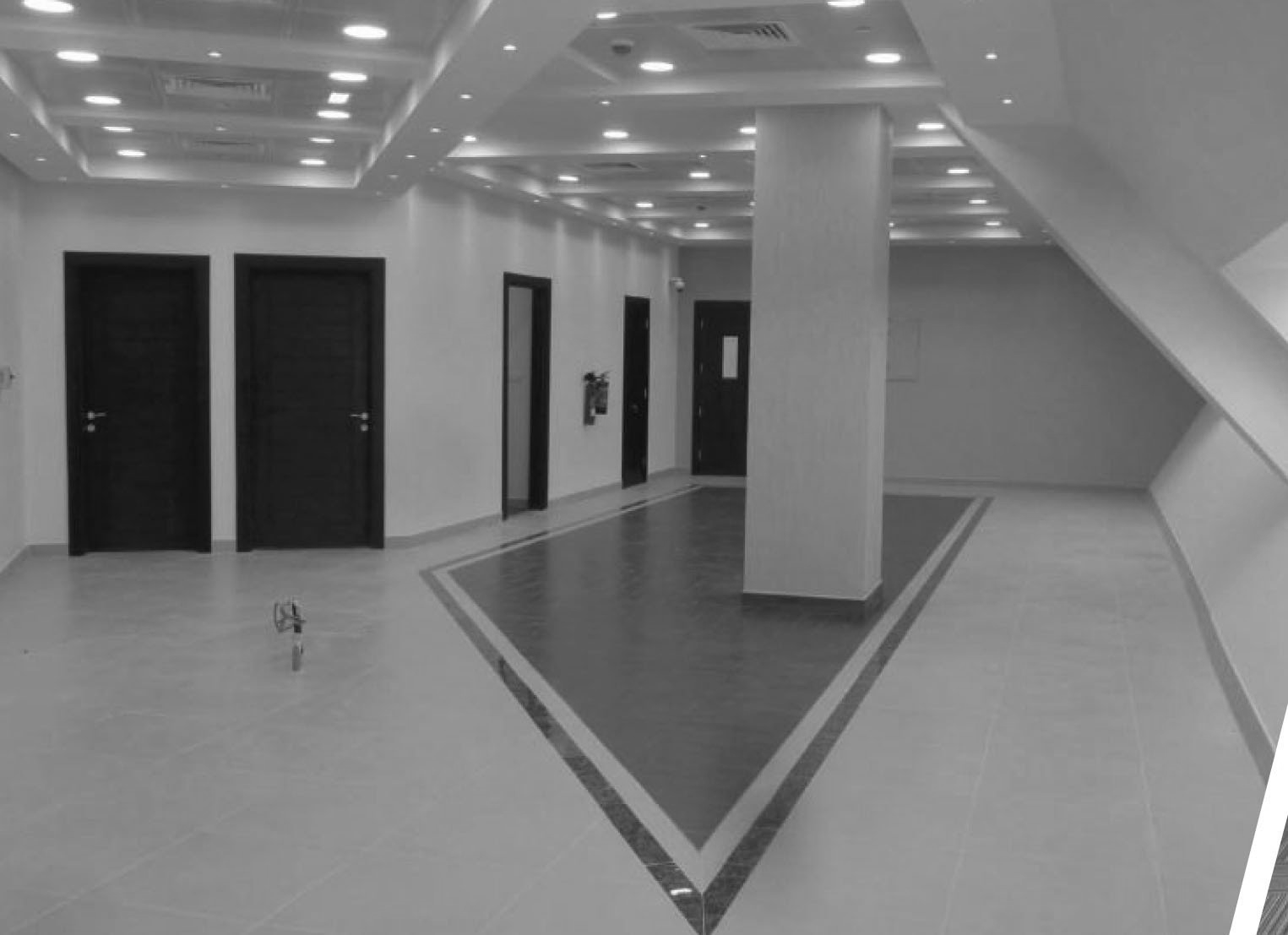Black and white interior hallway with multiple closed doors and a central support column. Geometric floor design.