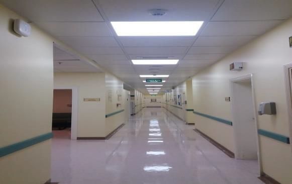 A long hallway in a hospital with a green exit sign on the ceiling.