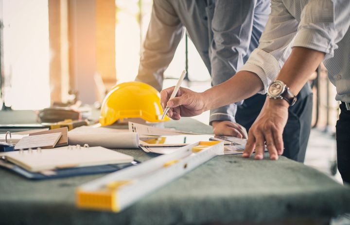 Two men are looking at a blueprint on a table.