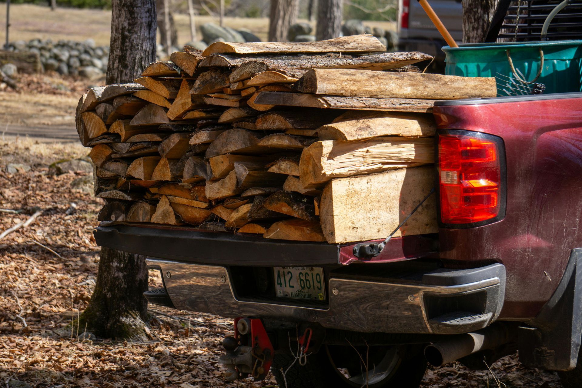 Wood stacked in the bed of a red pickup truck in a wooded area