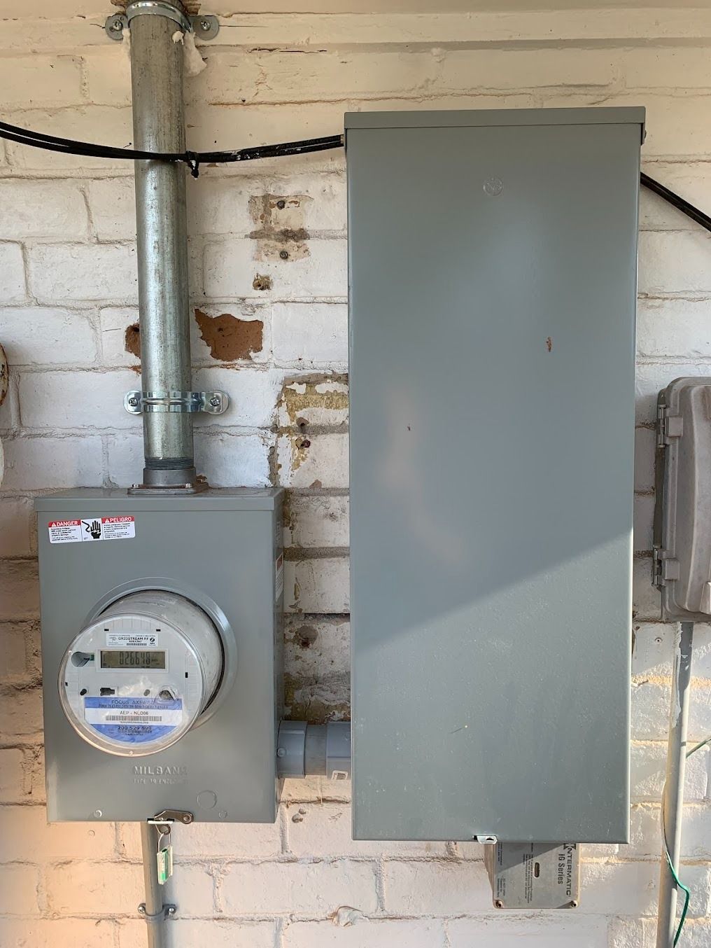 Two gray electrical boxes mounted on a painted brick wall with exposed conduit and wiring.