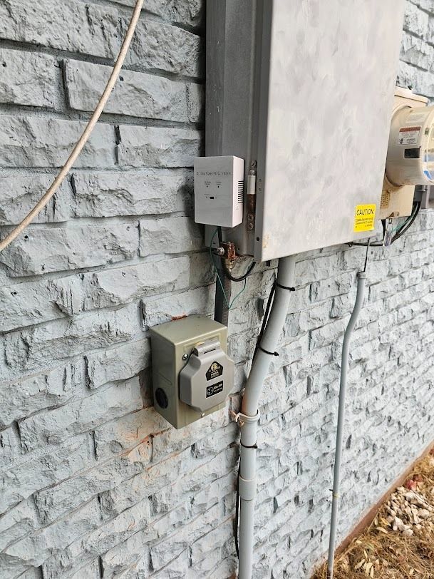 Utility meters and electrical boxes mounted on a gray brick wall outdoors.