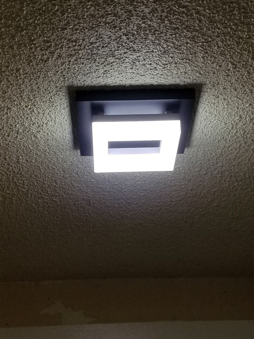 Ceiling-mounted square light fixture glowing against a textured ceiling