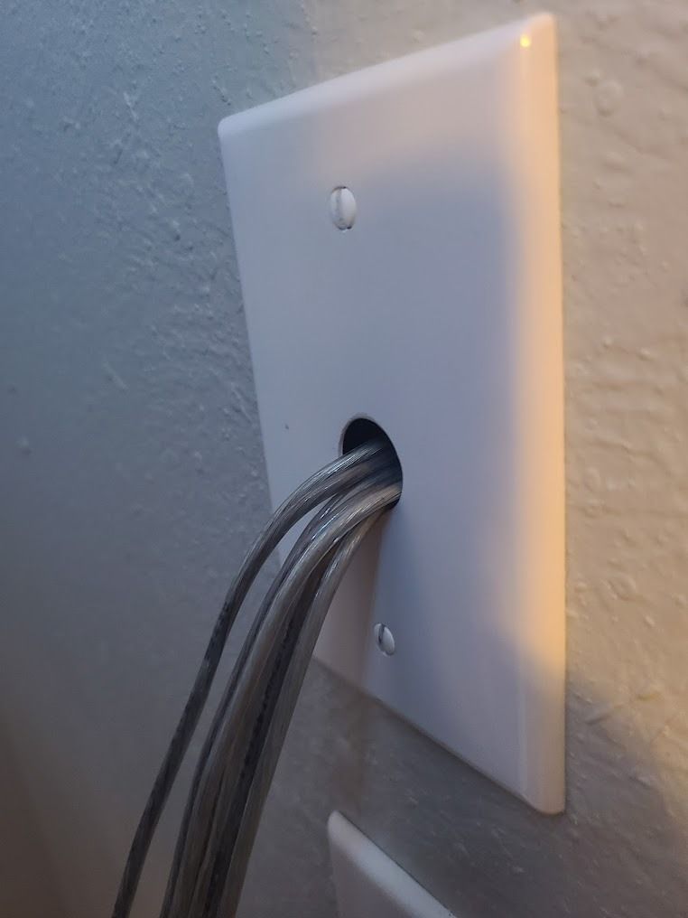 White wall plate with a hole, with gray cables passing through it.