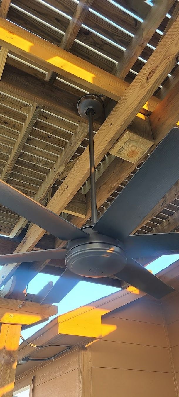 Large ceiling fan mounted under a wooden pergola, with warm sunlight filtering through the slats.