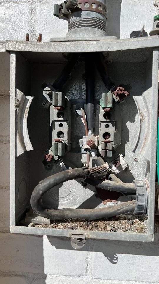 Open electrical junction box with exposed wiring, metal components, and a thick black cable inside.