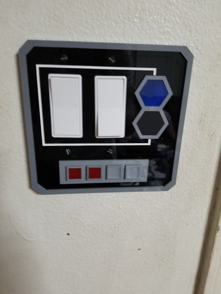 Wall-mounted black control panel with white switches and blue hexagonal buttons on a light wall