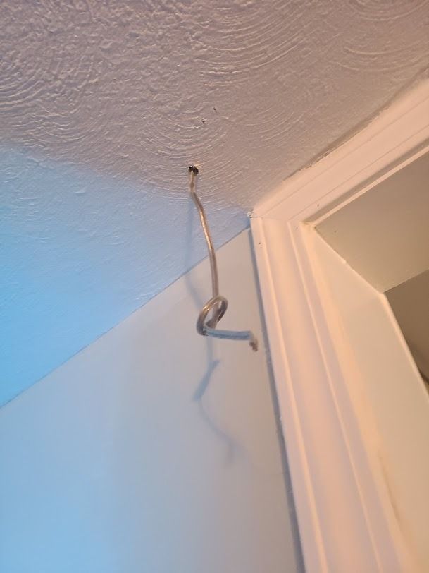A dangling metal hook hanging from a hole in the ceiling near a doorway