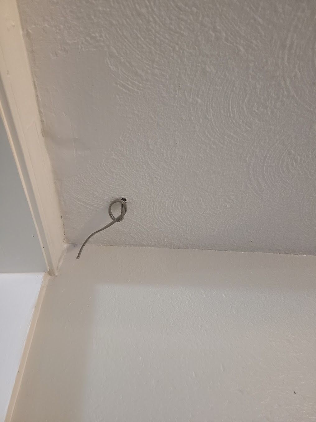 Ceiling corner with a loose wire and small opening in the white wall