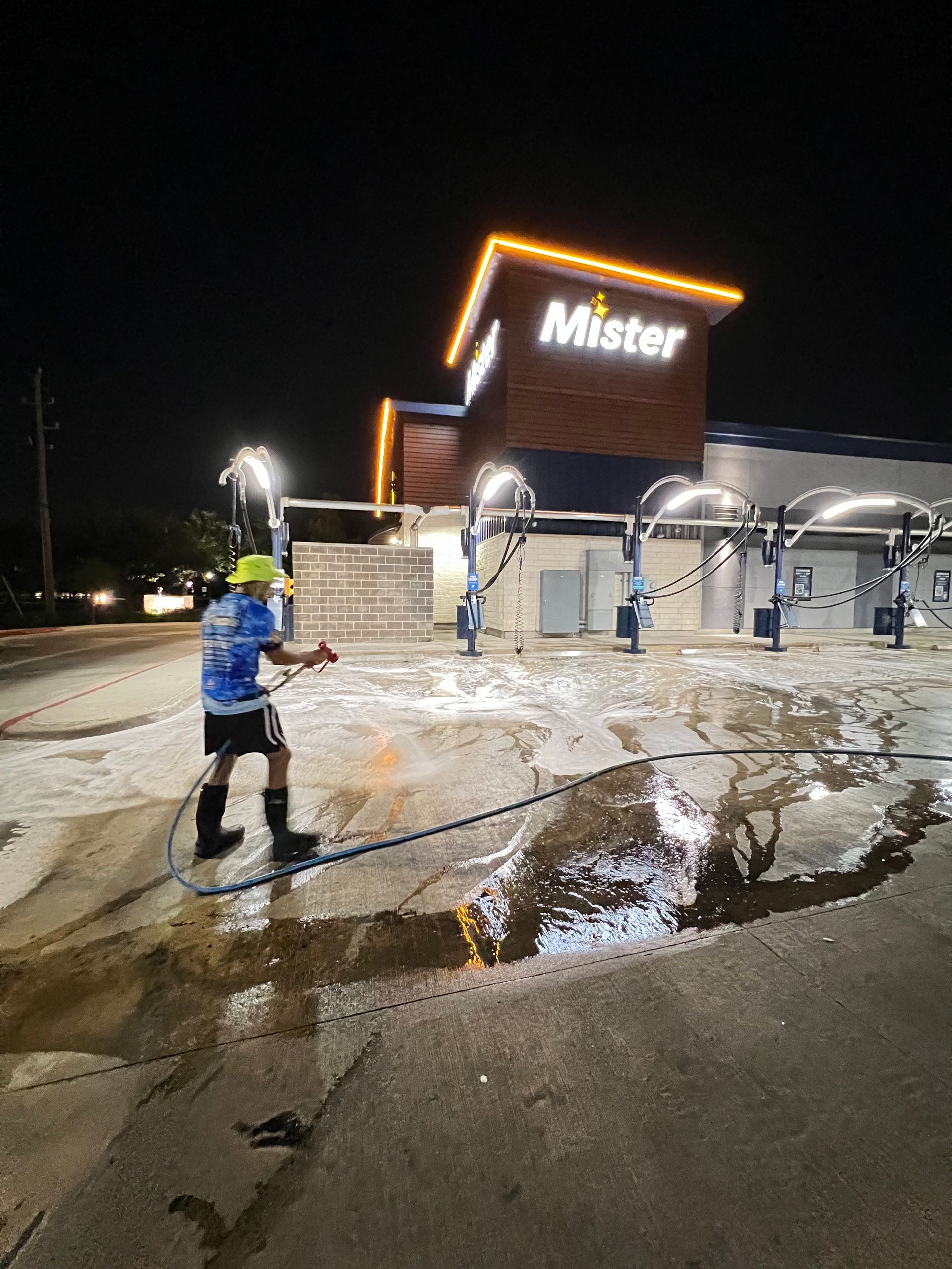 A person is cleaning a puddle in front of a mister car wash.
