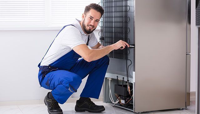 Un hombre está arreglando un refrigerador con un destornillador.