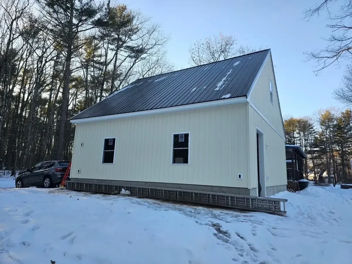 New construction building with light-colored siding, dark metal roof, and black framed windows in a snowy setting.