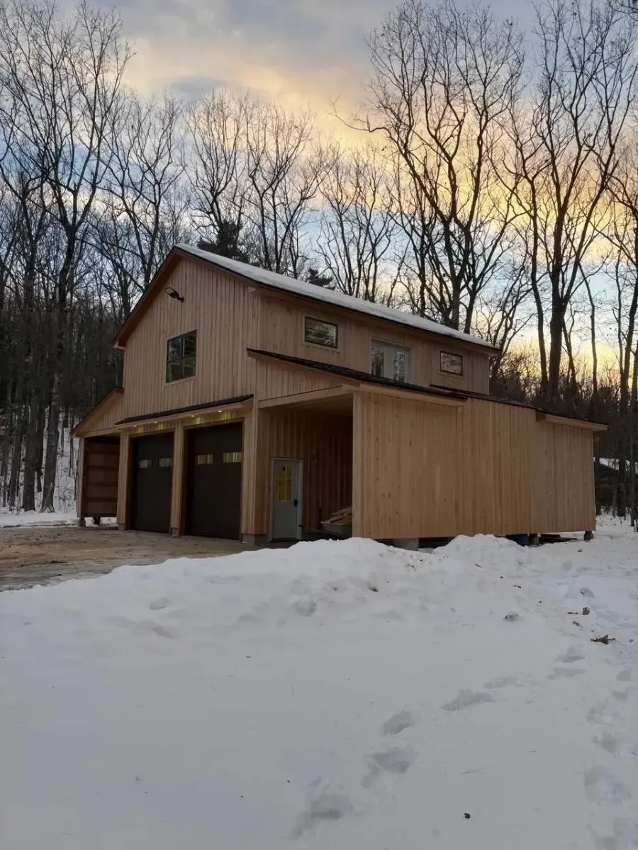 Wooden two-story building with three garage bays; snow on the ground, trees in the background.