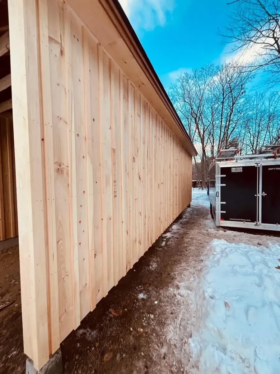 Wooden exterior wall of a building under construction, with snow on the ground and a blue sky in the background.