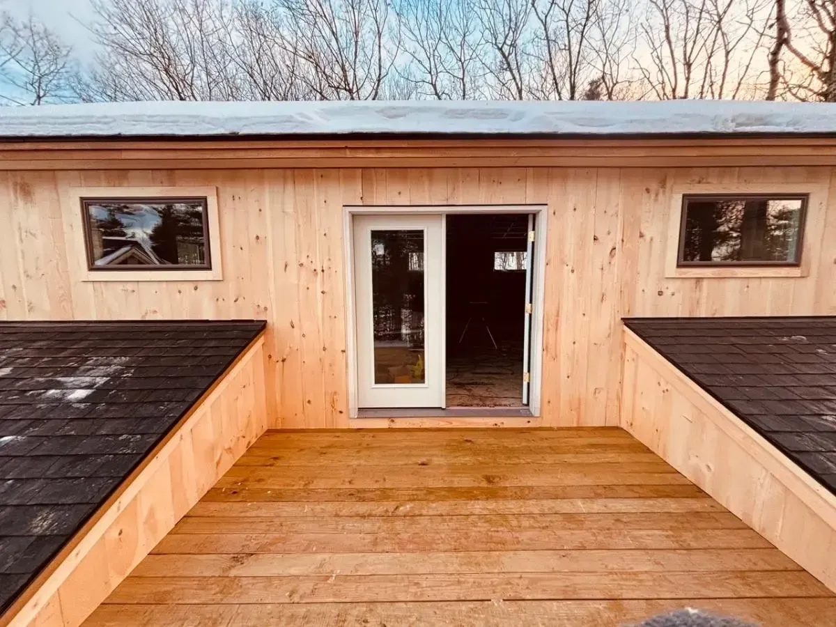 Wooden building with a deck, French doors, and two windows. Overcast sky in the background.
