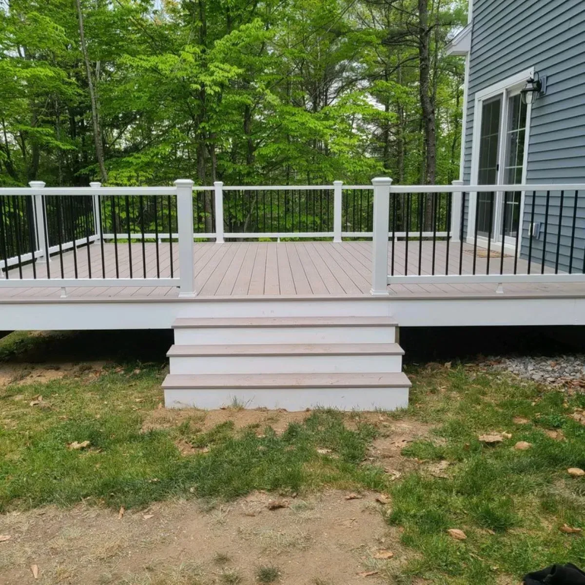 A deck with stairs and a white railing is in front of a house.