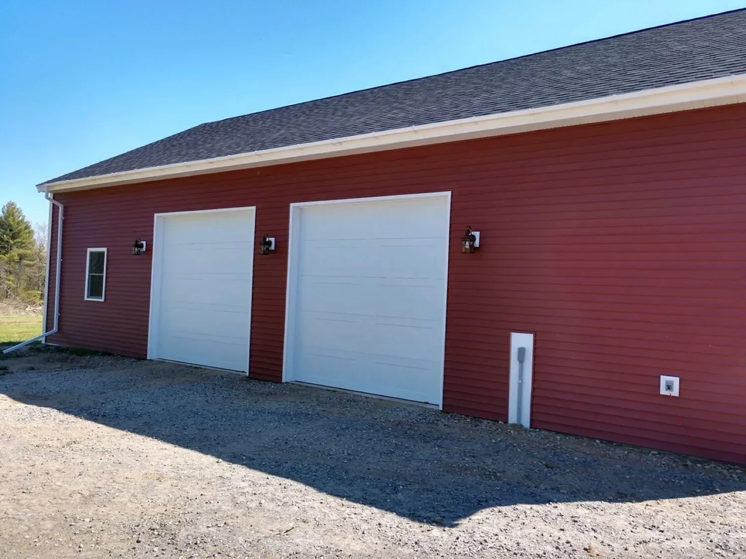 A red garage with two white garage doors and a blue sky in the background.