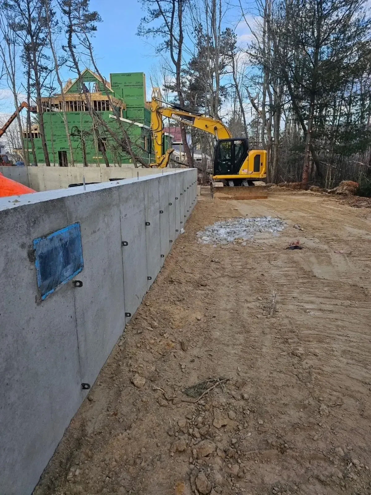 A construction site with a concrete wall and a yellow excavator.