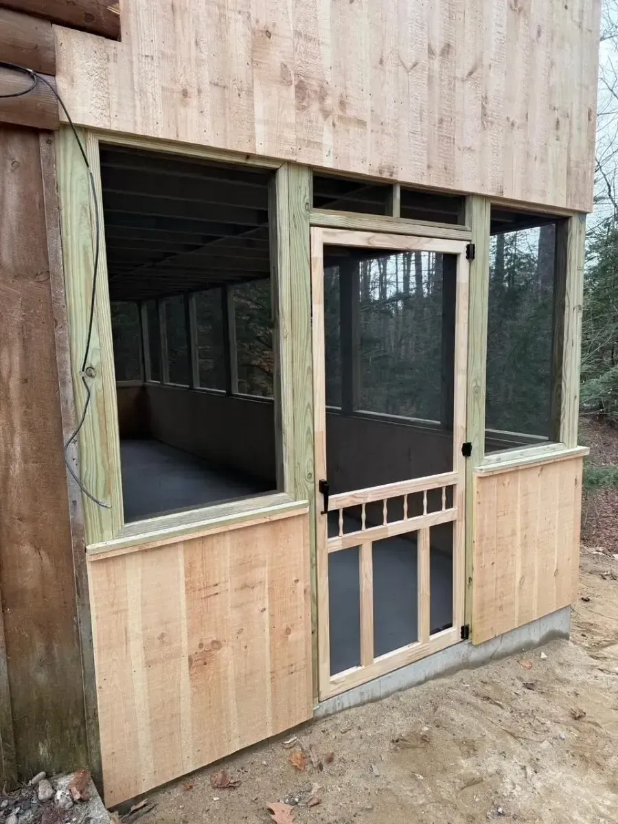 A screened porch with a door and windows made of light-colored wood.