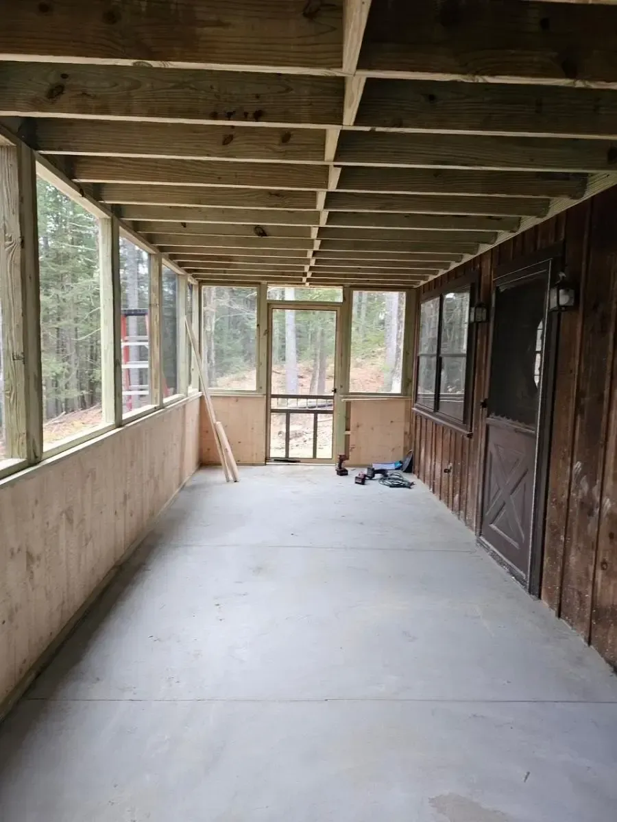 A screened-in porch with unfinished wood ceiling and walls, concrete floor, and screened windows.