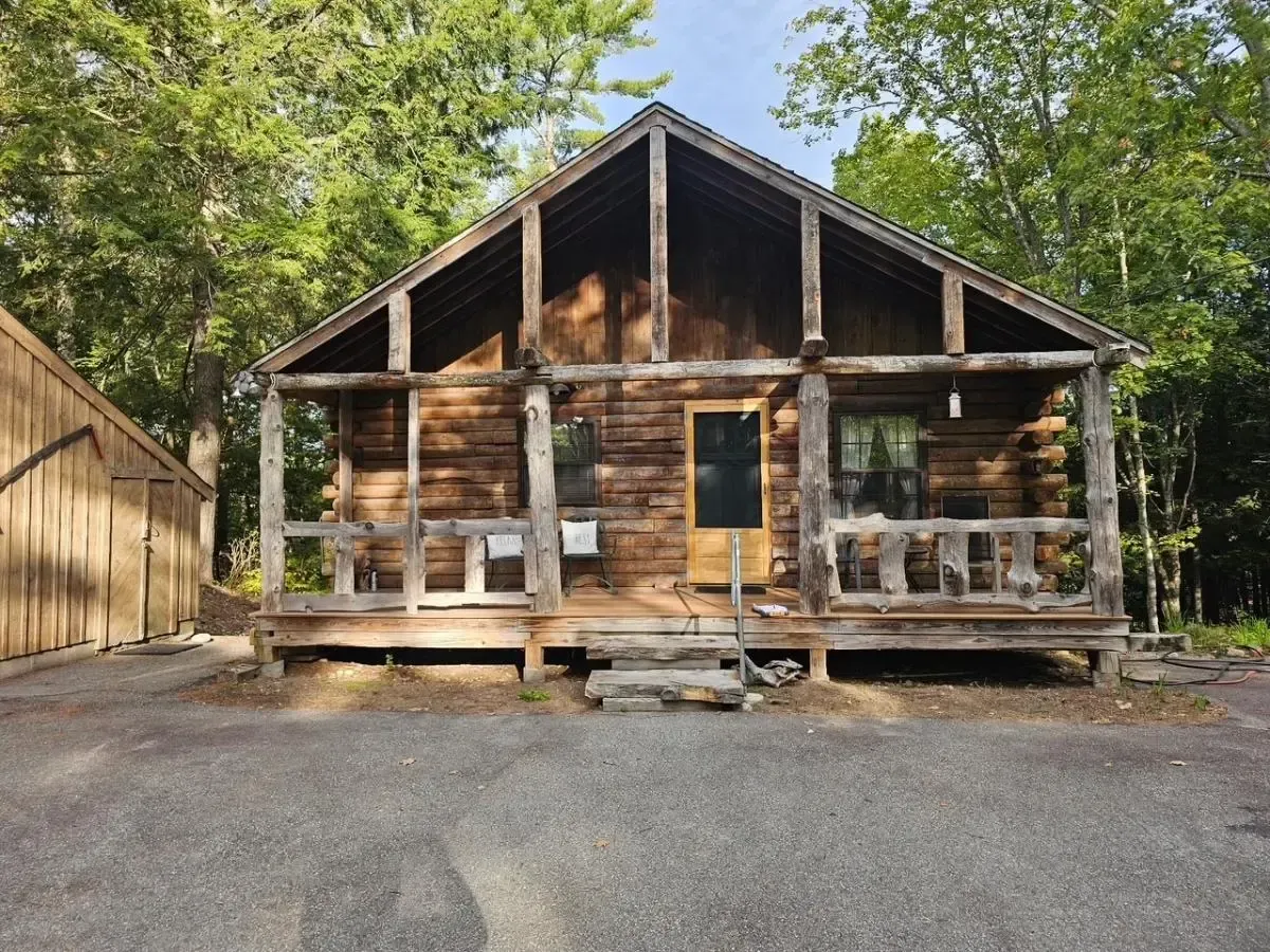 Rustic log cabin with porch, surrounded by trees.