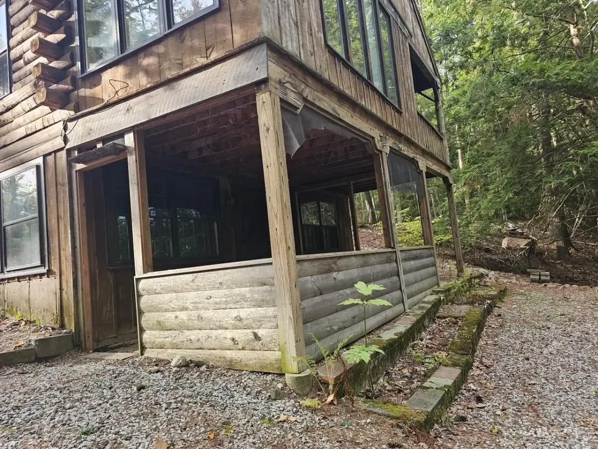 Log cabin with porch, surrounded by trees and gravel.