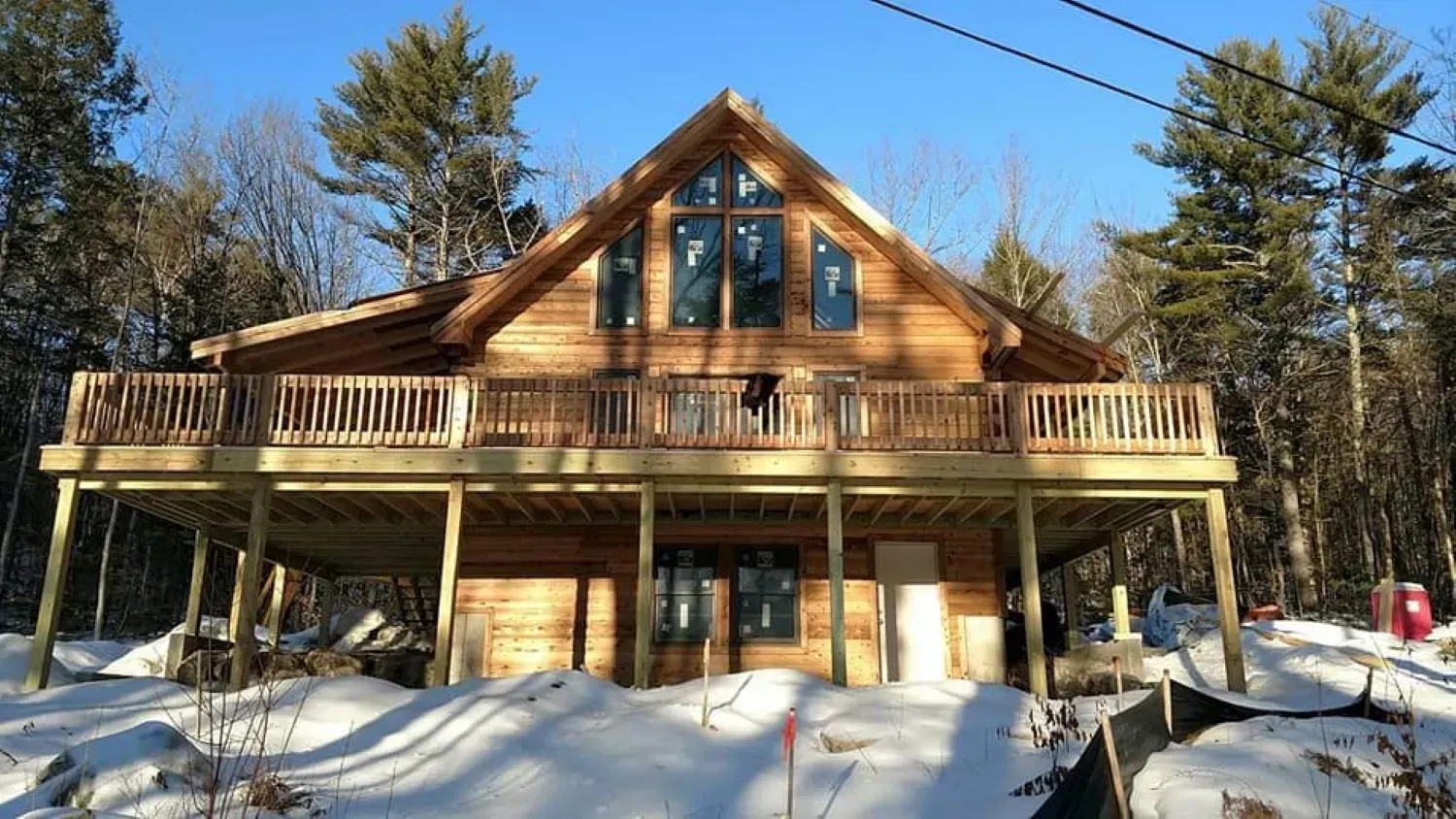 A large log cabin with a large deck is surrounded by snow.