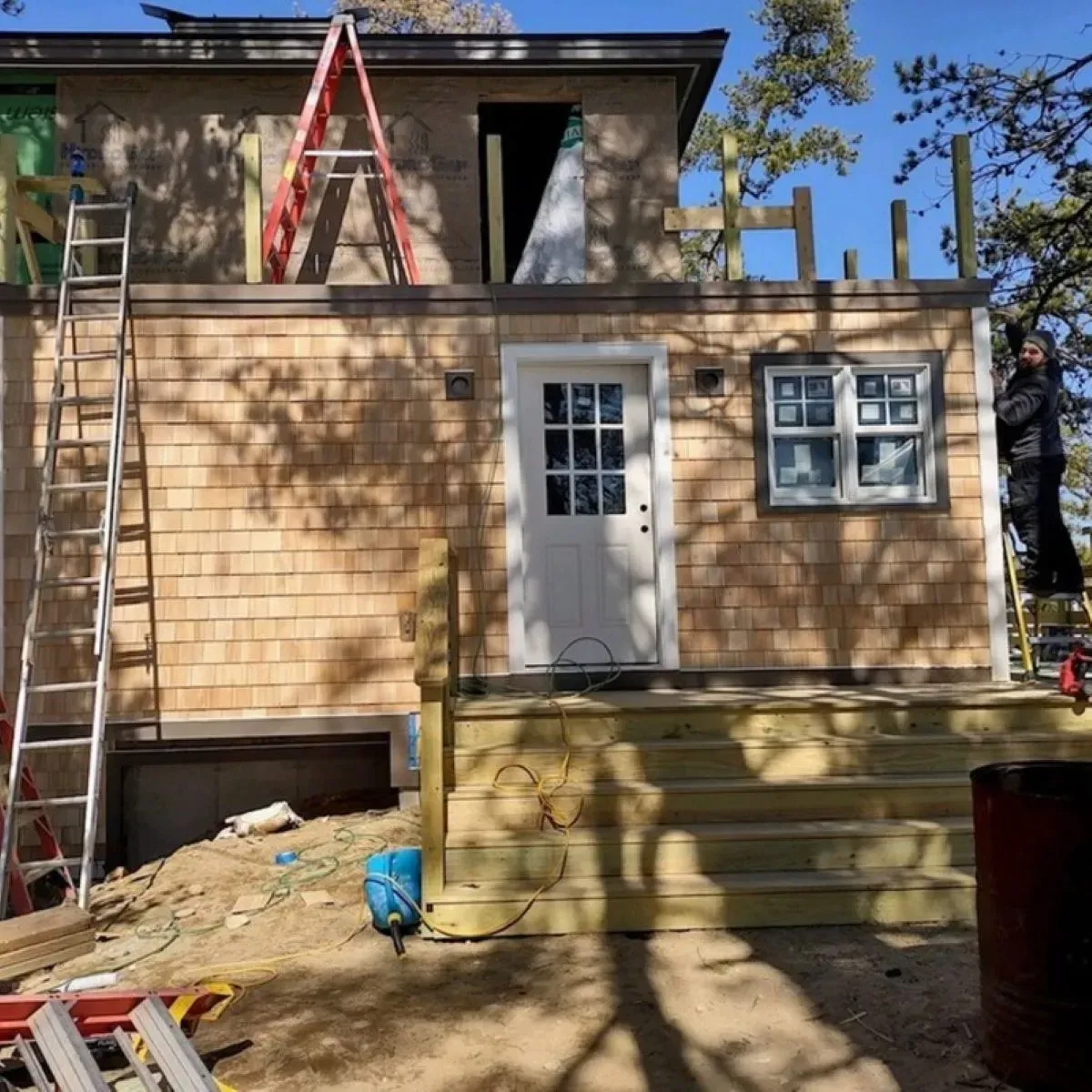 A man is standing on a ladder in front of a house under construction