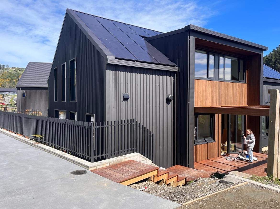 A man is sitting on a porch in front of a black house.