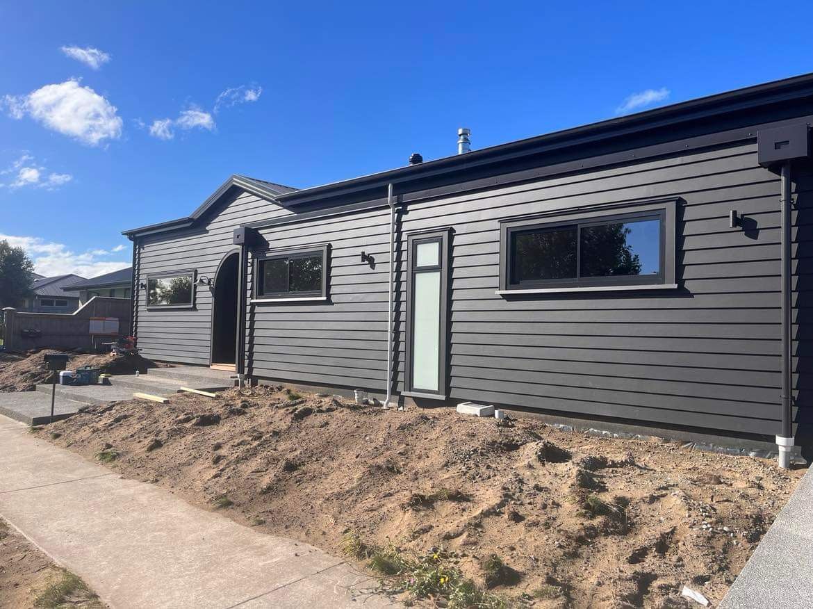 A black house with a lot of windows is sitting on top of a dirt hill.