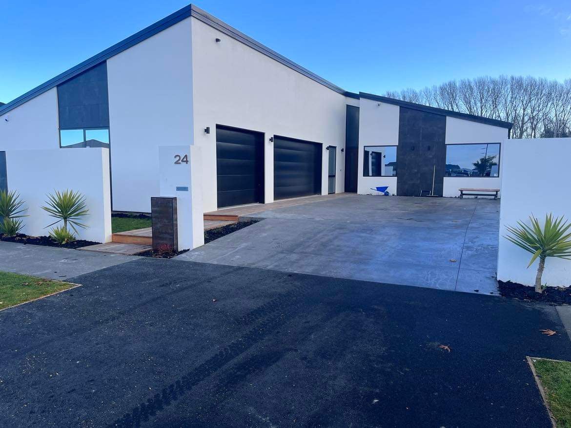A large white house with black garage doors and a black driveway
