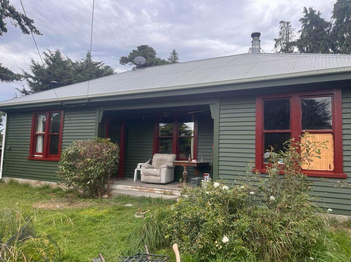 A green house with red trim and a chair on the porch.