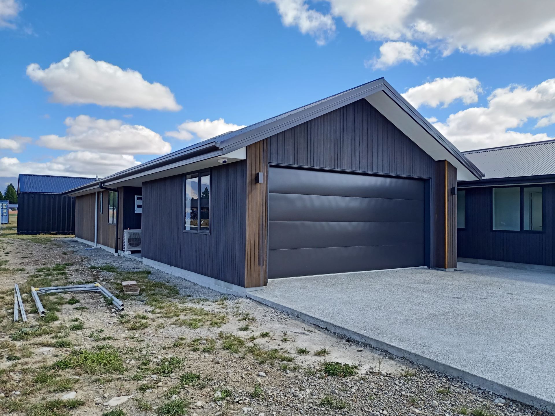 A black house with a garage door is sitting on top of a dirt field.