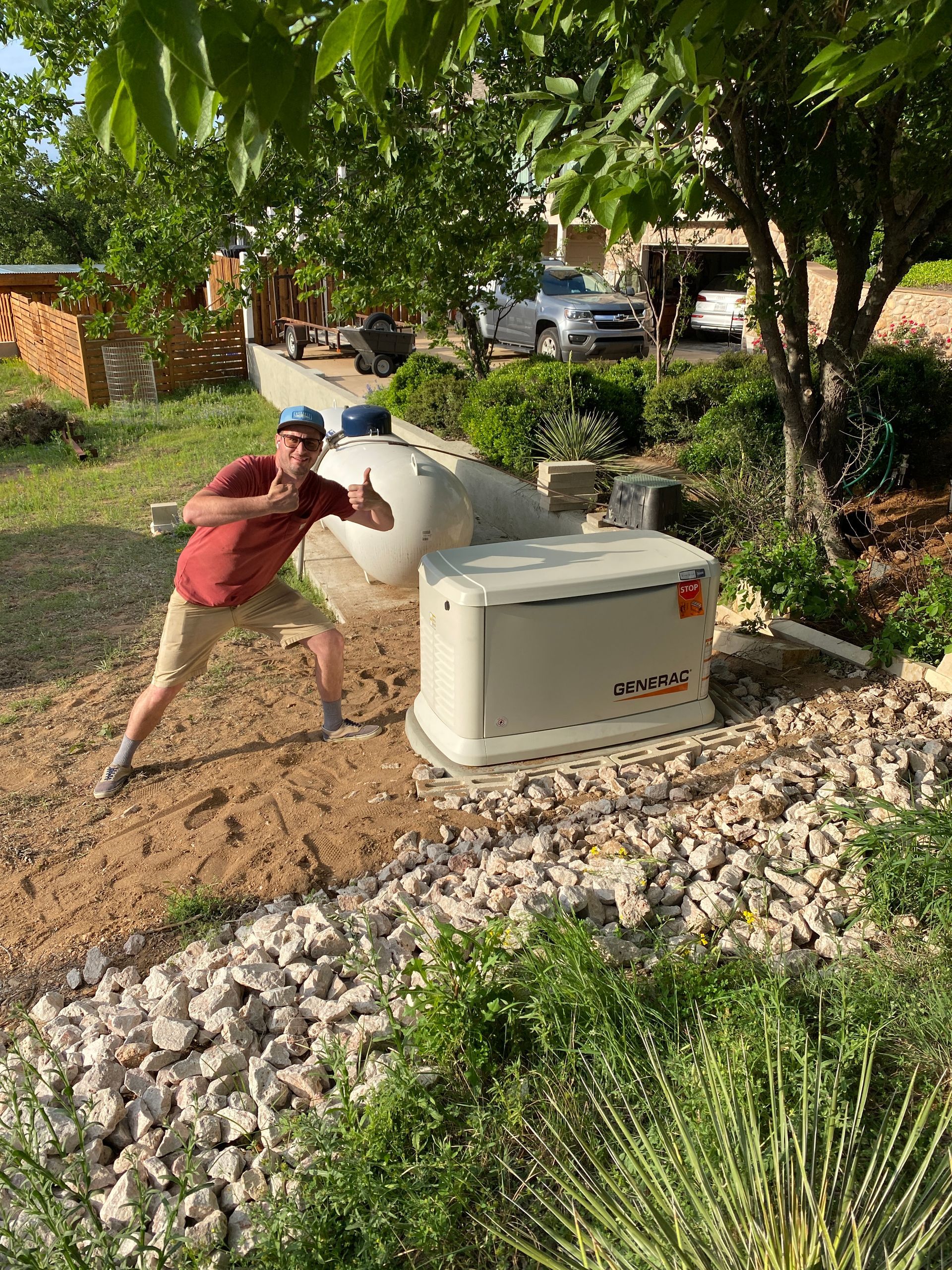 A man is standing in front of a generator in a yard giving a thumbs up.
