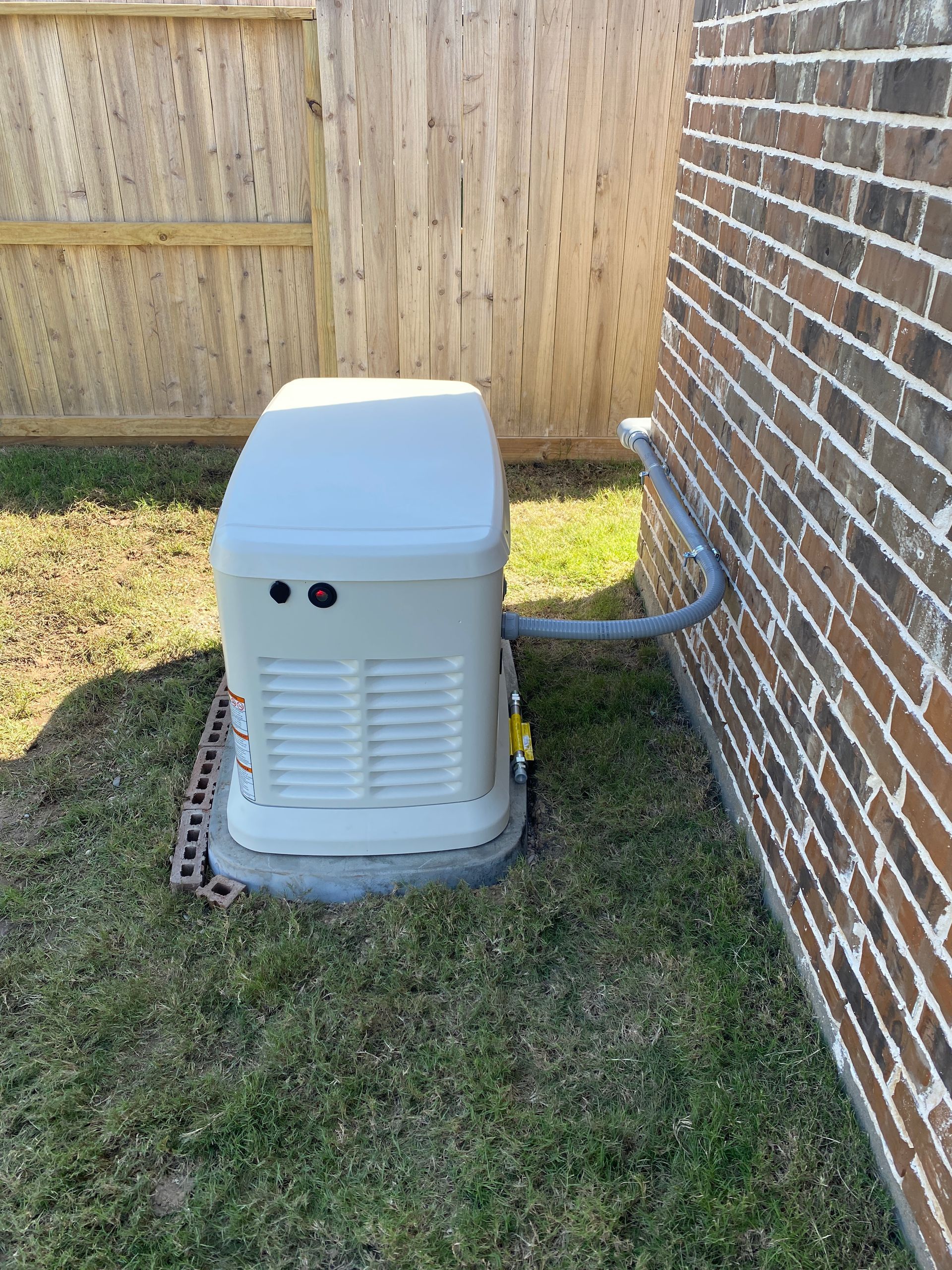 A white generator is sitting on the side of a brick building.