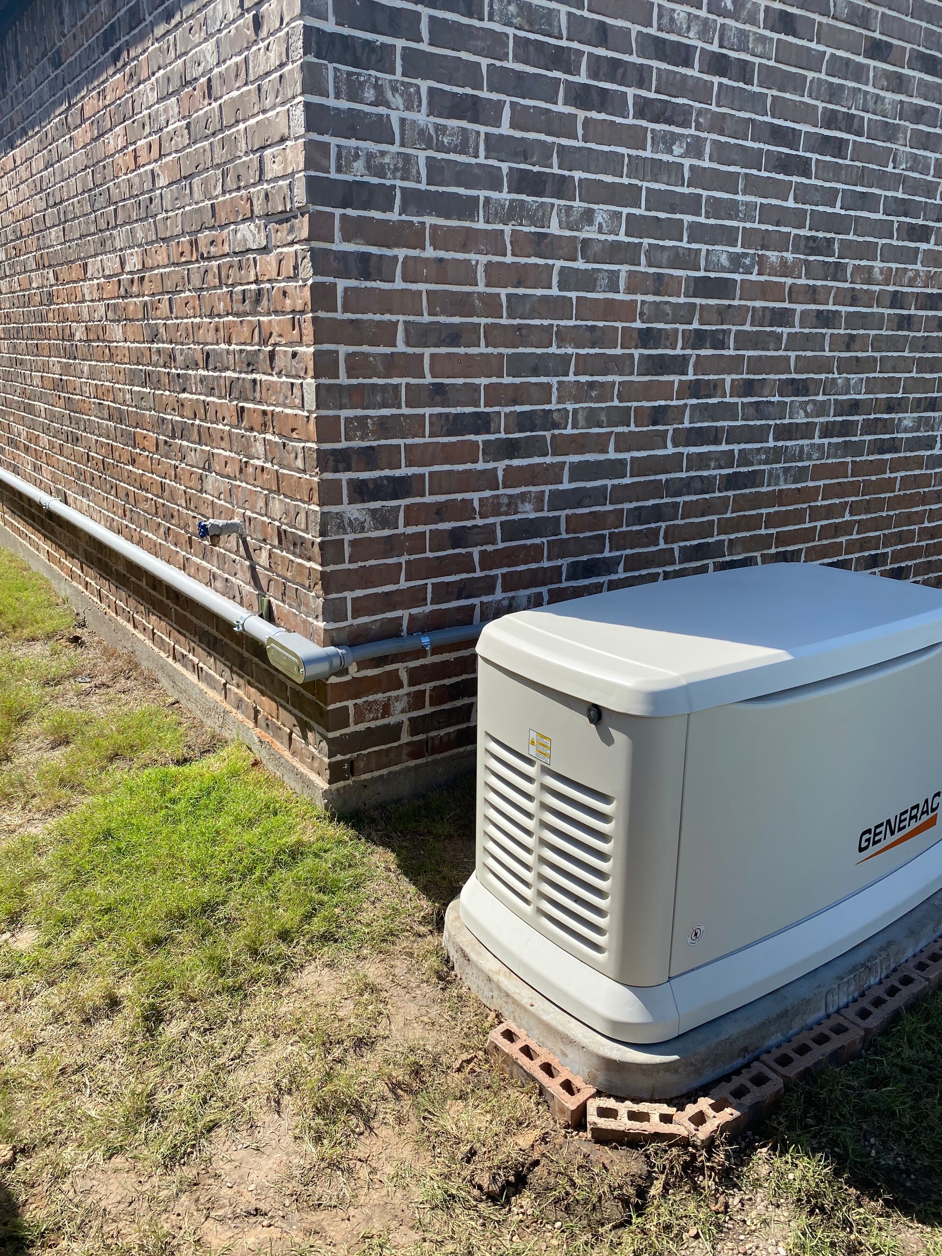 A generator is sitting on the side of a brick building.
