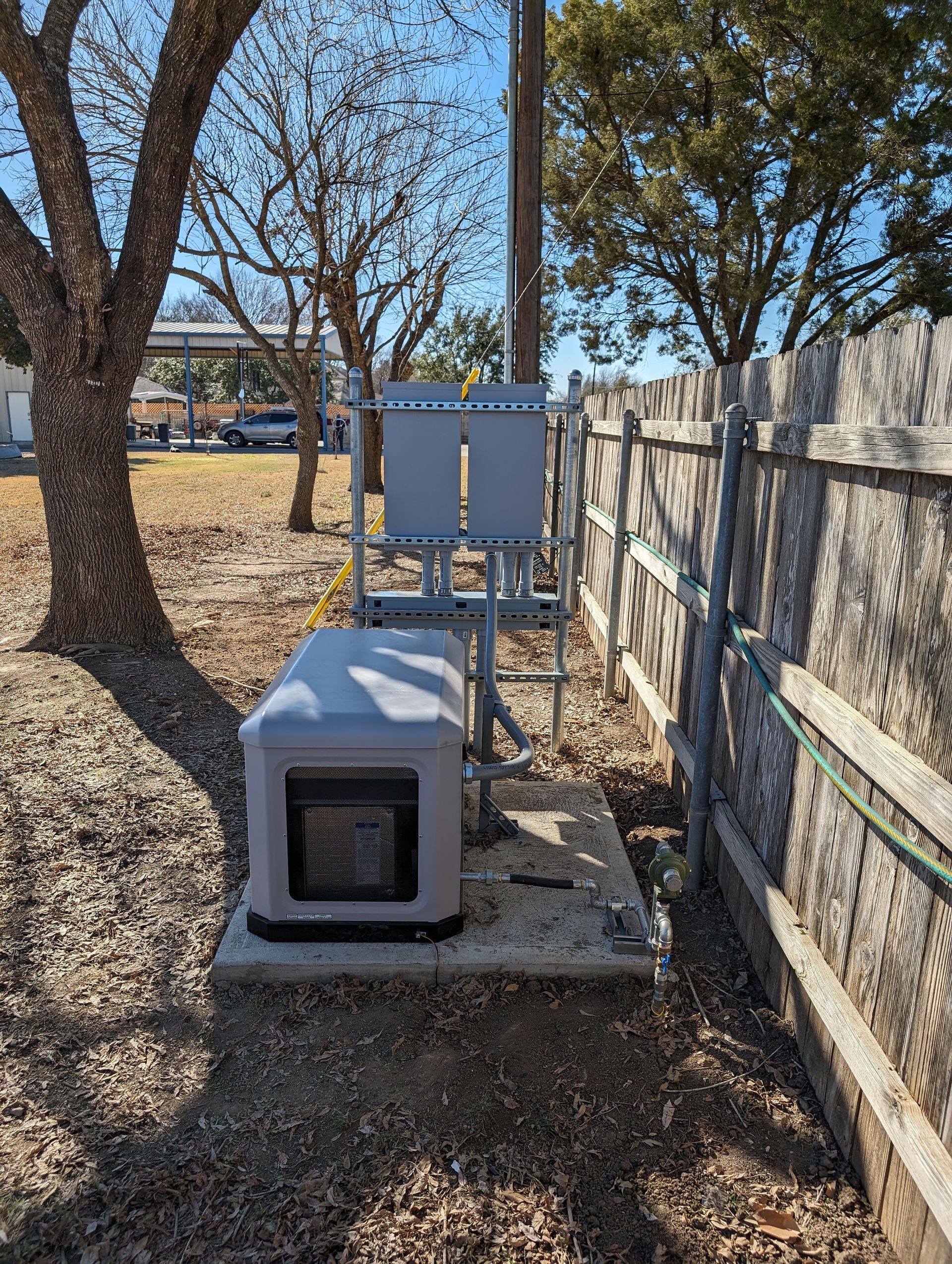 A generator is sitting next to a wooden fence in a backyard.