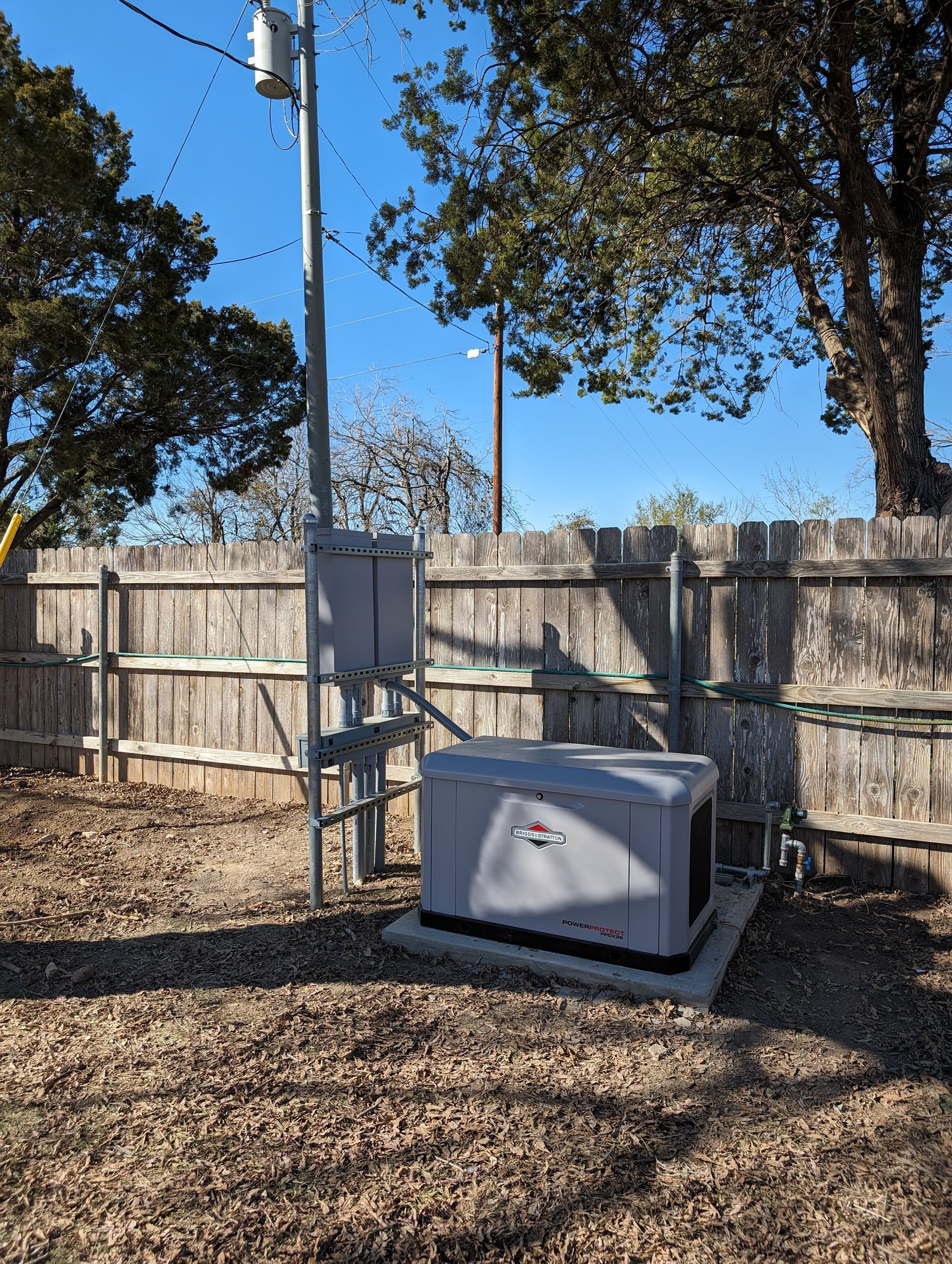 A generator is sitting in the dirt in front of a wooden fence.