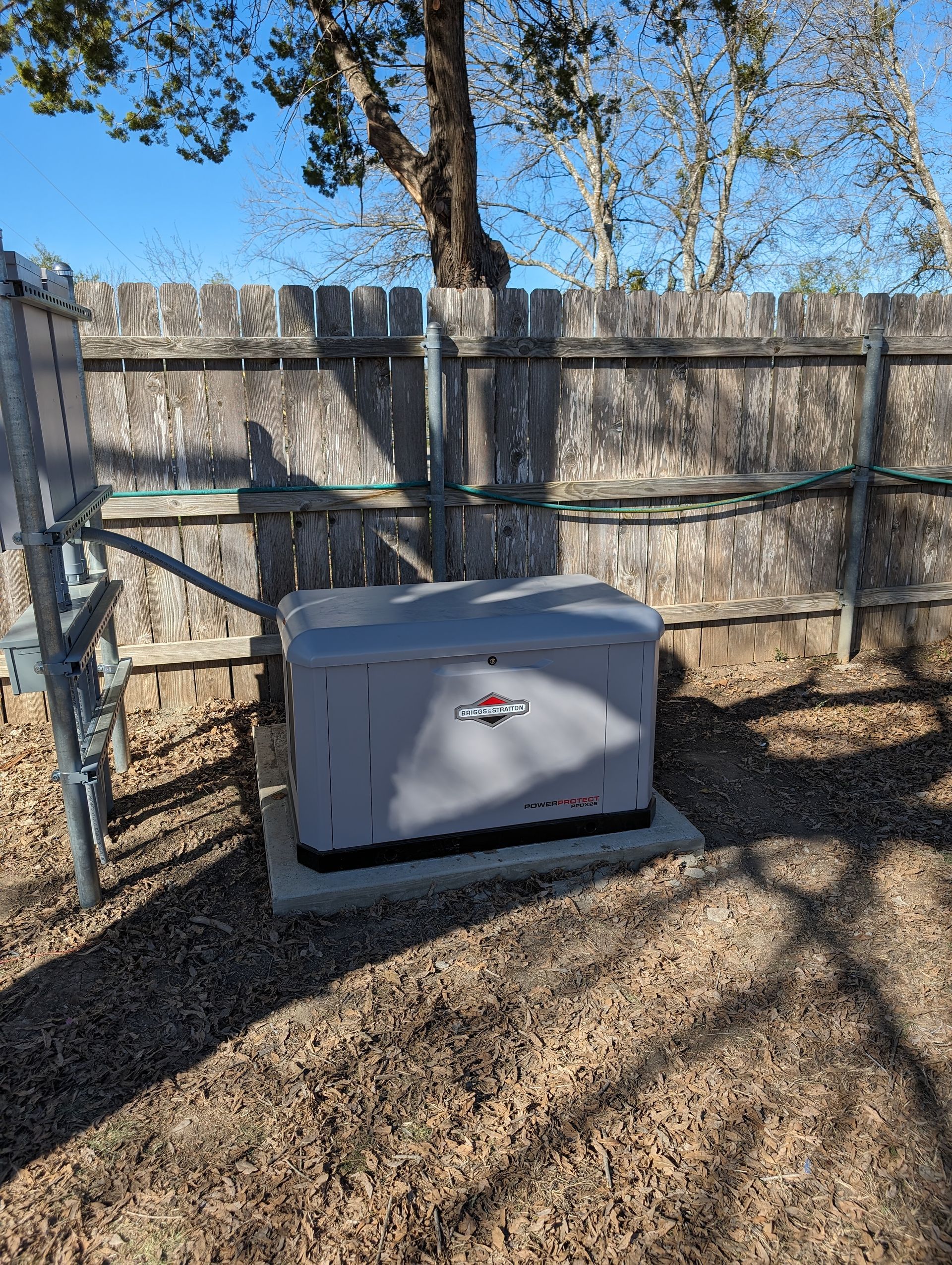 A generator is sitting in the dirt in front of a wooden fence.