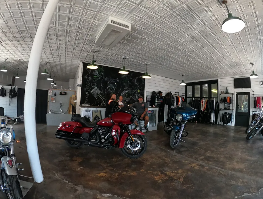 Motorcycle showroom with red and blue bikes on display, customers near central counter, patterned ceiling.