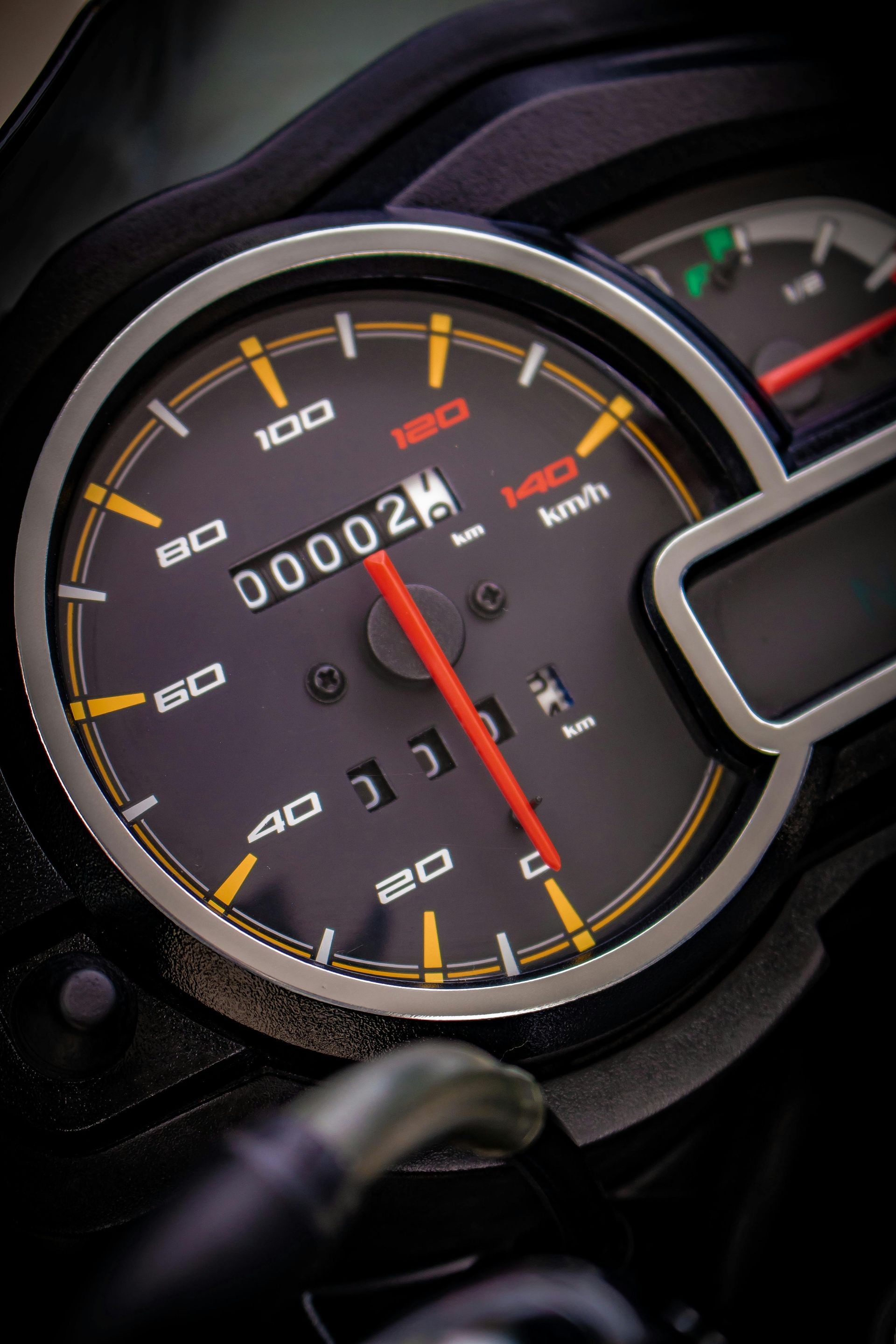 Motorcycle speedometer showing a speed of 2 km/h and an odometer reading of 2. Black and orange.