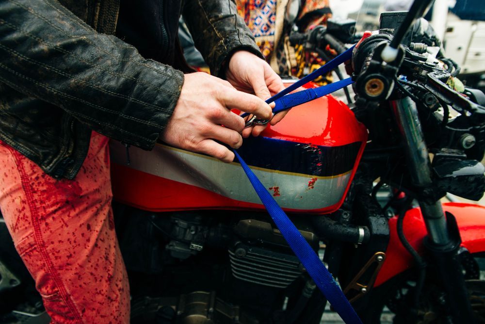 Person adjusting blue straps on the red and silver gas tank of a motorcycle.