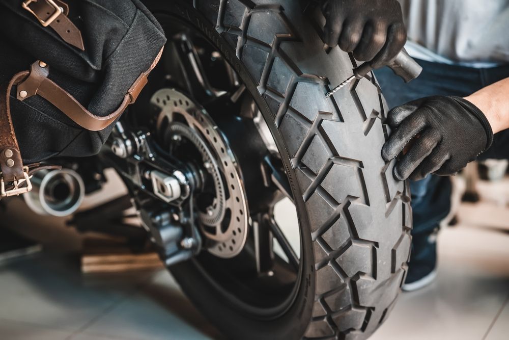 Person wearing gloves inspecting a motorcycle tire.